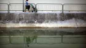 A woman pushing a baby buggy is reflected in a monsoon drain on Friday, Oct. 12, 2012, in Singapore.