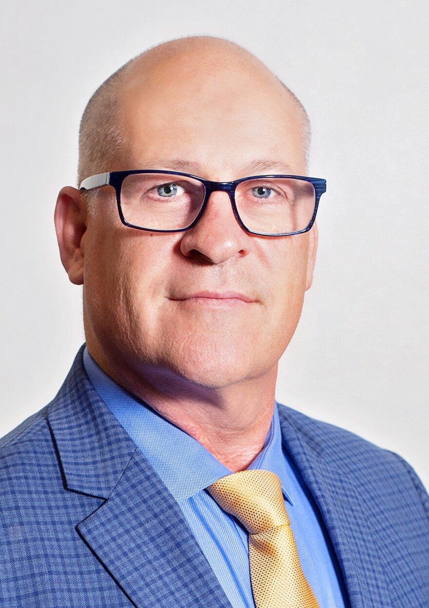 Jim Hammond wearing black glasses, blue jacket and yellow tie