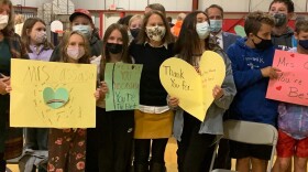 Middle schoolers line up with signs and an adult woman is in the center.