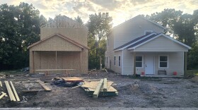 Two houses sit at a construction site. The one on the right is almost finished, while the one on the left still needs exterior paneling and a roof.