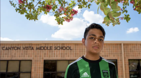 Kid stands in front of school in an Austin FC shirt