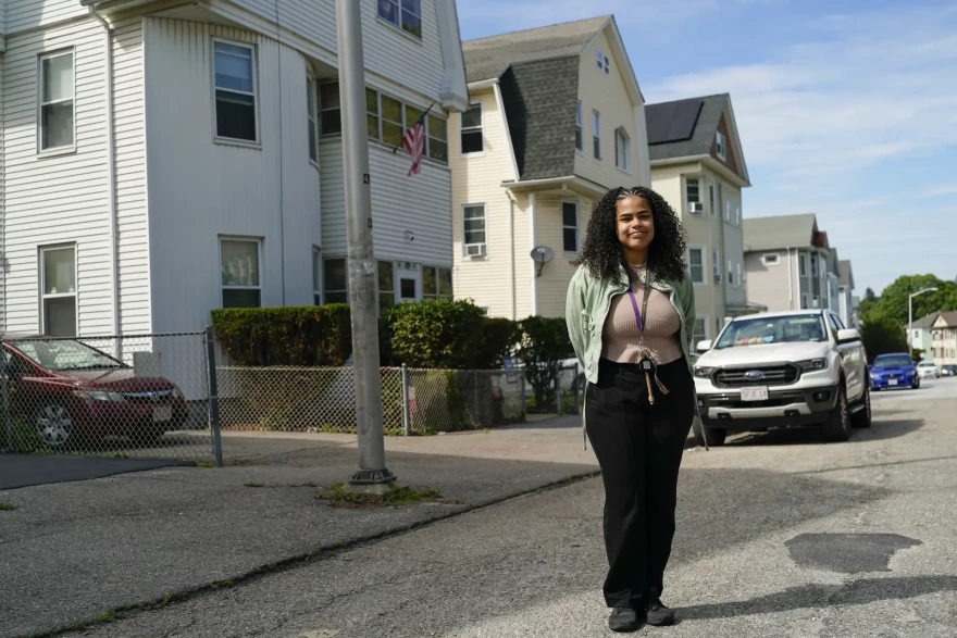 A woman stands in front of several houses on a city street.