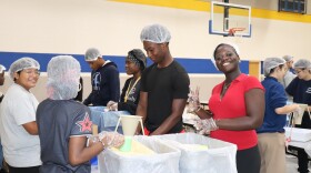 A group of students don hair covers and gloves as they scoop food into packages.