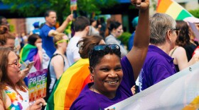 Woman raises her fist with a smile in a crowd of people and rainbow flags. 