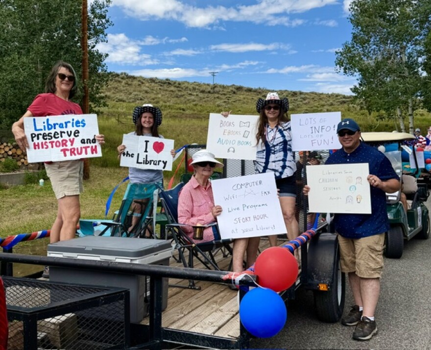 A group of people standing in a truck bed holding signs that say "Libraries preserve history and truth," and "I heart the library"