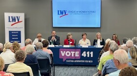 Republican hospital board candidates sit on a panel. Crowd of people watch them.