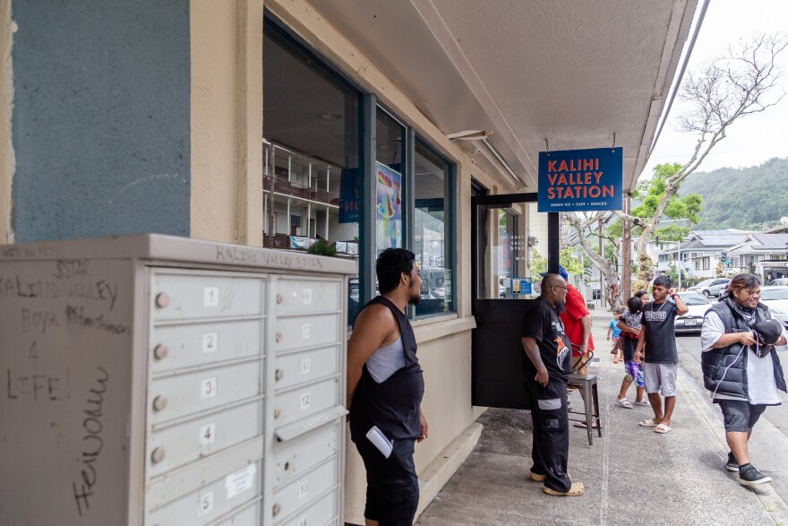 Residents wait outside the Kalihi Valley Station as their phones charge from a portable battery, located inside the station. (August 17, 2026)