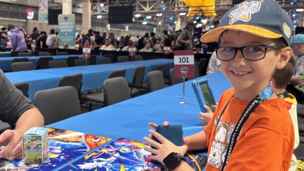 A boy sits at a blue table with a deck of trading cards