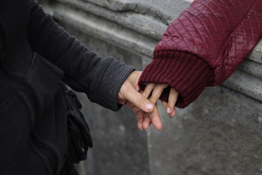 A woman holds a young girl's hand.