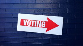 Sign that says Voting with an arrow hanging on blue brick wall