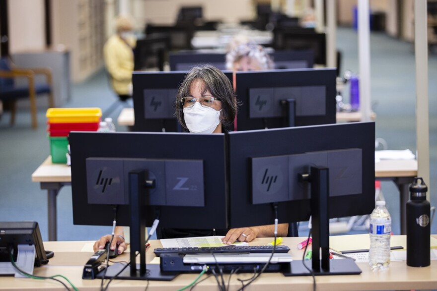 Masks are required, temperatures are checked, and workers are kept far apart as they count ballots for the Aug. 4 primary.