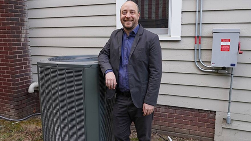 Kevin Kircher leans on an outdoor unit of an air-source heat pump. He said groundsource heat pumps — also known as geothermal heat pumps — are more efficient than air-source because the temperature underground tends to be more stable.