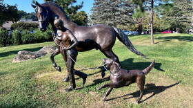 Statue of a girl walking a horse alongside a running dog.