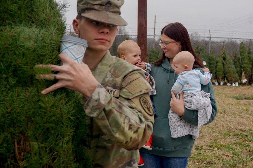 Cpl. Noah Rodriguez grabs a free Christmas tree at Fort Leonard Wood while his wife, Cheyenne, looks on while holding their children, Braxton and Paisley.