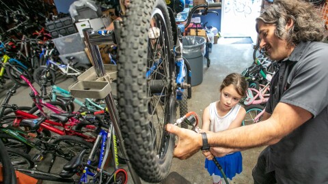 Cameron Berg, 7, helps Norte Chief Bike Mechanic Tyler Wituszynski inflate the tires on a bicycle she and her mother Beth Alexander of Washington, D.C., pick up for lessons on Wednesday from the Norte Wheelhouse Bike Library in Traverse City.