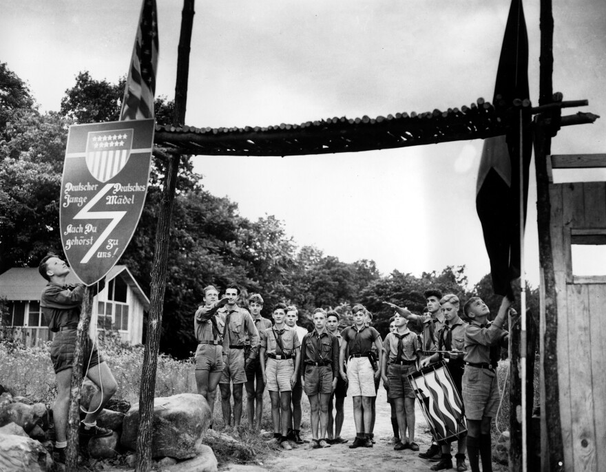 Youths at a German American Bund camp stand at attention as the American flag and the German American Youth Movement flag, right, are lowered in a ceremony at sundown in Andover, N.J., July 21, 1937. One person plays the drum, right, and two people make the Hitler salute.