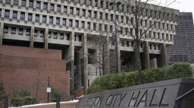 A stone sign that reads Boston City Hall is outside of a building in Boston