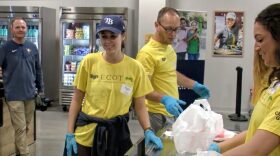 People wearing tshirts and gloves work with food. 