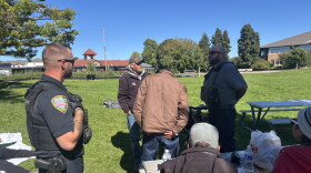 Traverse City Police Officer Matthew Kirkey and Police Support Services Worker Brad Neuder explaining the department's new enforcement efforts to a table of homeless individuals at Hull Park (Credit: IPR News / Maxwell Howard)