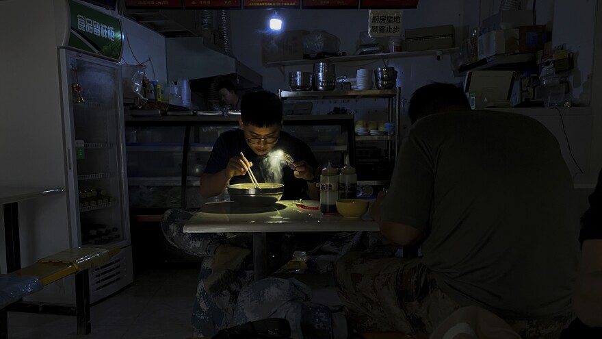 A man uses his smartphone flashlight to light up his bowl of noodles as he eats breakfast at a restaurant during a blackout in Shenyang, in northeastern China's Liaoning province, Wednesday. People ate breakfast by flashlight and shopkeepers used portable generators as power cuts imposed to meet official conservation goals disrupted manufacturing and daily life. [Olivia Zhang / AP]