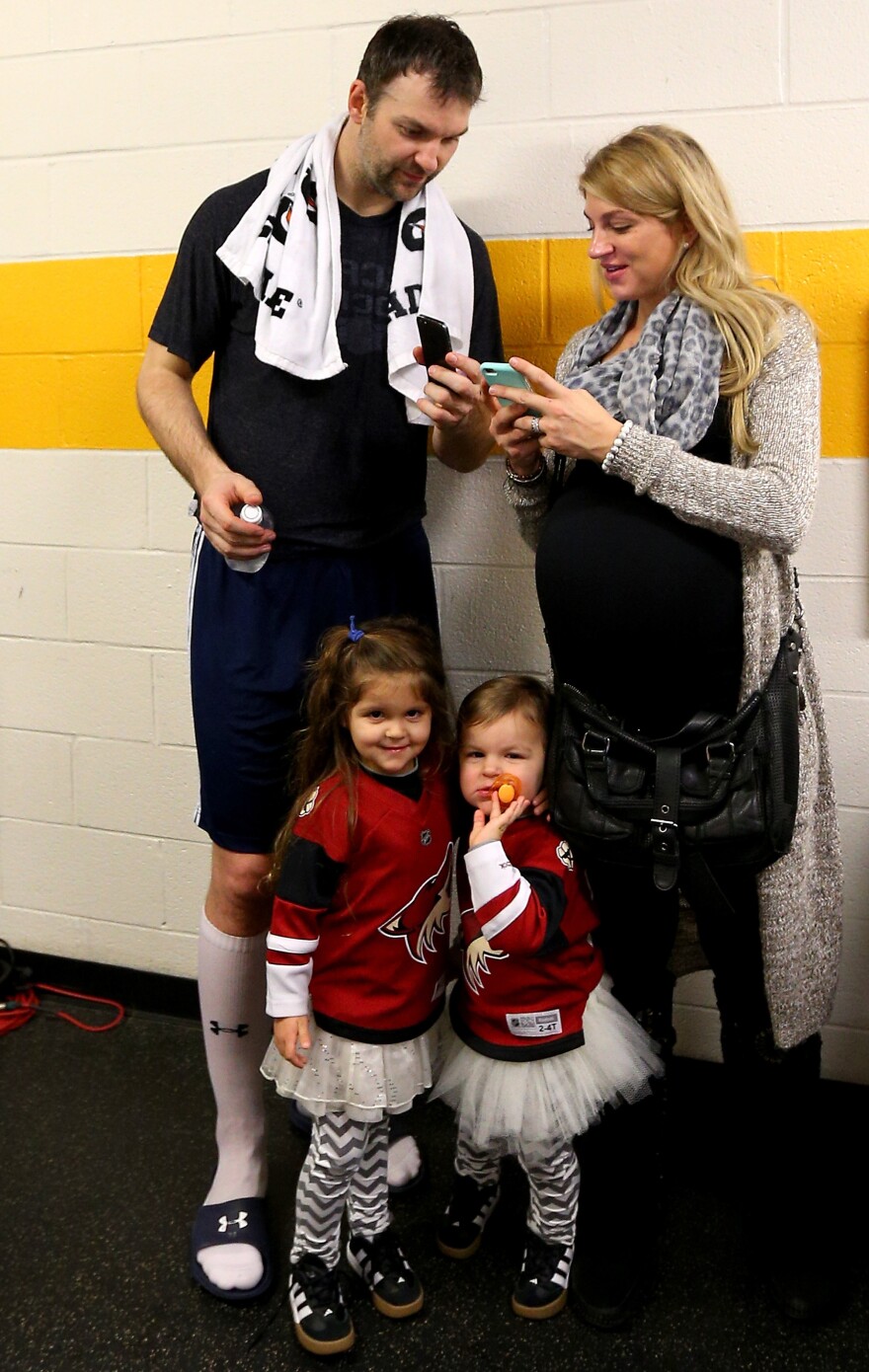 John Scott talks with his wife, Danielle, after the 2016 NHL All-Star Game, as their kids amuse themselves.