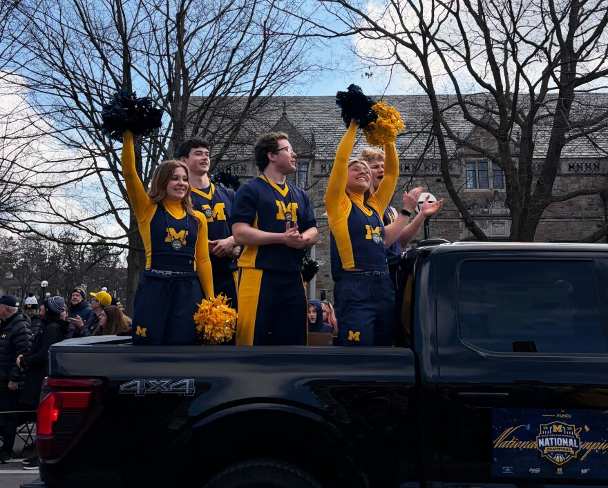 Michigan cheerleaders in maize and blue uniforms cheer with the crowd as the parade begins.