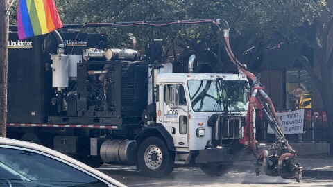 A large truck labeled "Liquidator" affixed with a power washer sprays water on a street.