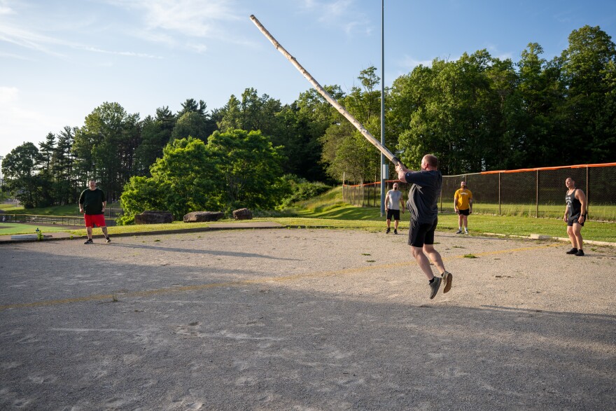 man throwing large log while others watch.