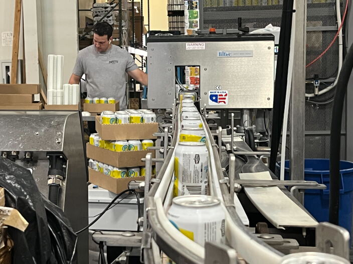 A line of cans going through a machine to get labeled with a yellow and white sticker with a barcode. 