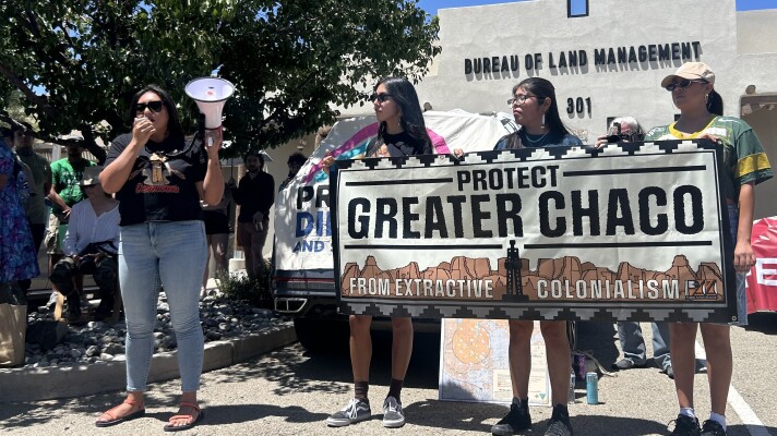 Pueblo Action Alliance Executive Director Julia Bernal (left) speaks out against proposed changes to Chaco Canyon protections while PAA members hold a banner