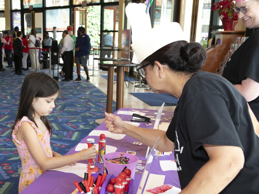 A teaching artist helps a young girl decorate a paper hat