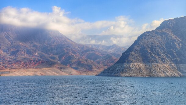 A wide shot of Lake Mead and the surrounding mountains. The sky is blue and clouds are hanging at the mountain peaks. 