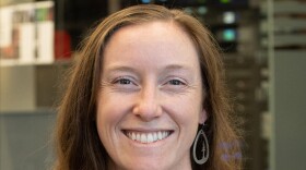 A smiling woman with brown hair wearing a gray dress.