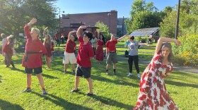  Several people all dressed in red stand in a park with their right arms extended over their heads