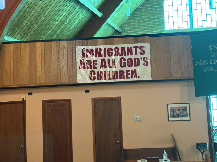 A sign hangs in the back of a church sanctuary that reads "Immigrants are all God's Children."
