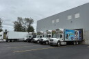 Outside of a warehouse with six food distribution trucks parked outside of it 