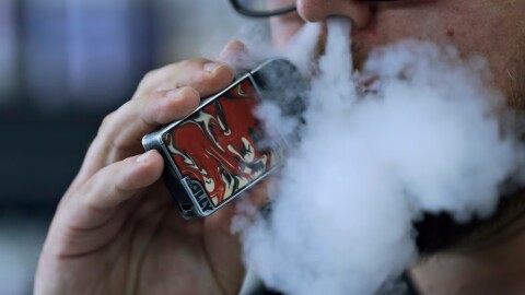 FILE - In this Friday, Oct. 4, 2019 file photo, a man using an electronic cigarette exhales in Mayfield Heights, Ohio. A judge has cleared the way for Montana to temporarily ban the sale of flavored e-cigarettes and other flavored vaping products. State officials say they plan to implement the ban Wednesday, Dec. 18, 2019.