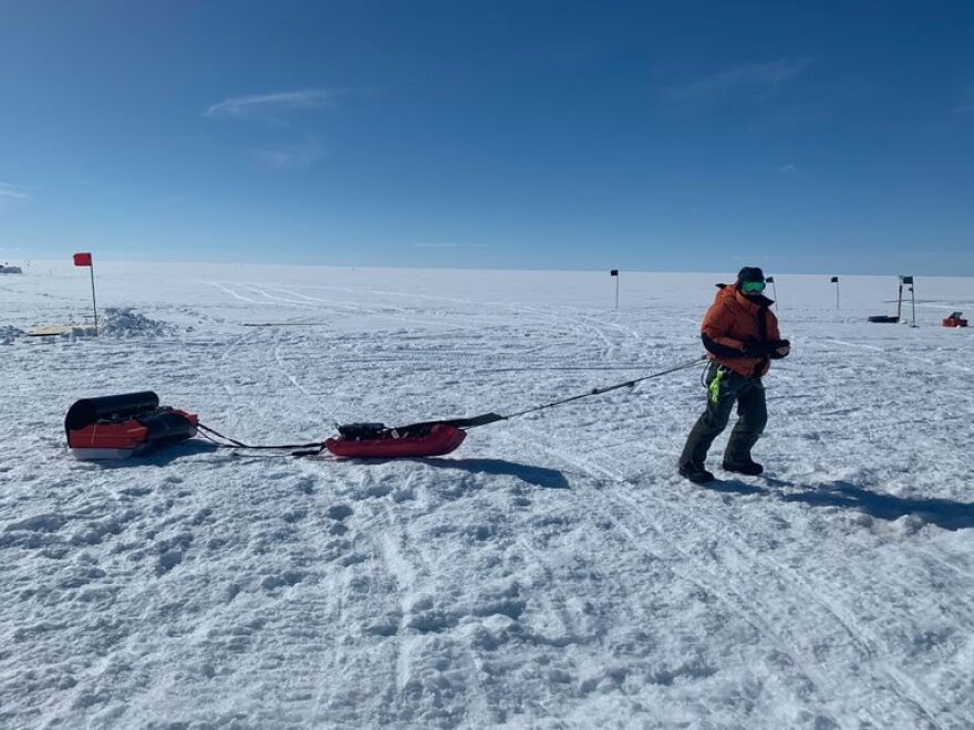 A person in red and black snow gear stands on a snowy, icy expanse.