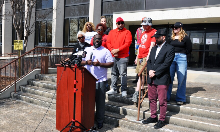 Eric Hall, a community activist and organizer with the Southern Workers Assembly, stands behind a podium surrounded by workers at a press conference in front of Central Alabama Water's headquarters in February.