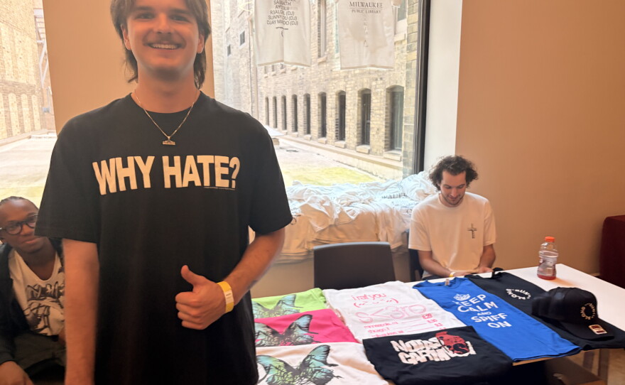 Nolan Busalacchi, the founder of the Milwaukee-based record label Run Along Forever, poses in front of a table full of merch for guests to purchase at The Library Show.