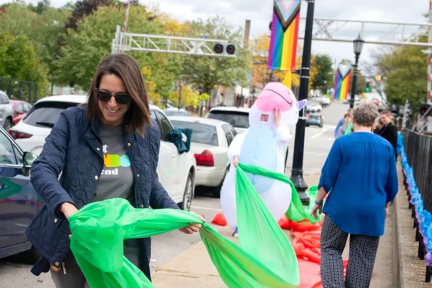 A woman decorates a sidewalk with rainbow streamers