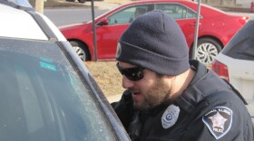 A police officer leans onto the driver's side of a car, speaking with that driver. 