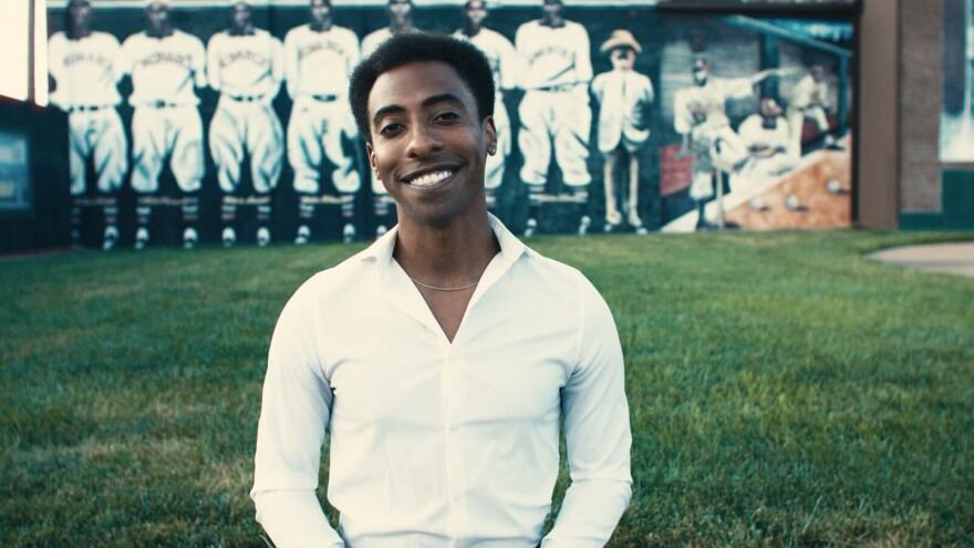 A man in a white button down stands in front of a mural