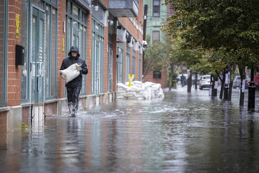 A person is seen walking through water carrying a white bag full of sand.