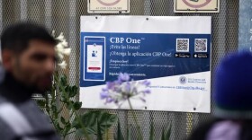 People waiting to apply for asylum stand in front of a sign for the CBP One app as they camp near the pedestrian entrance to the San Isidro Port of Entry, linking Tijuana, Mexico with San Diego.