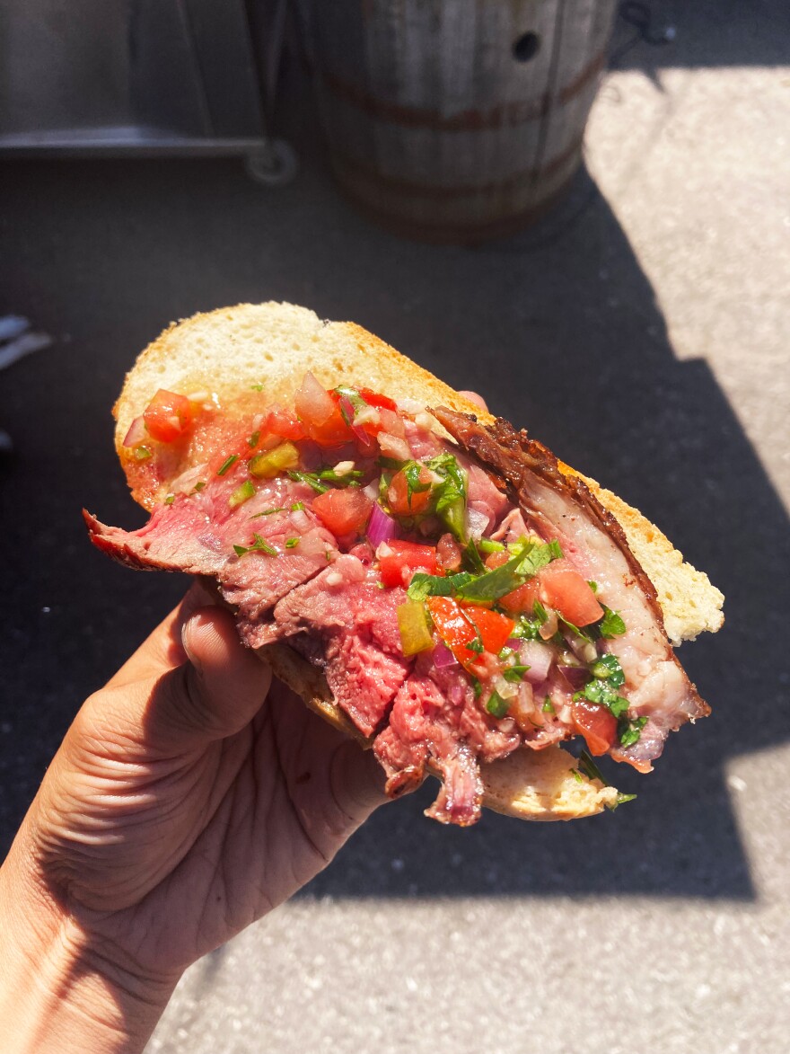 a hand holds a slice of bread with steak and salsa on top