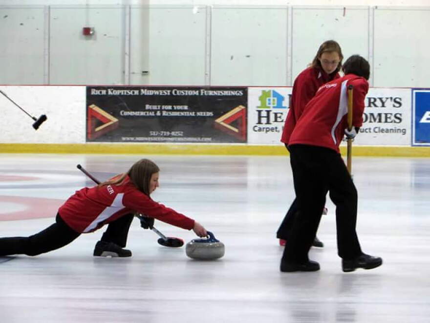 Stephanie Senneker slides the stone at the USA Arena Curling National Championships. Pam Nelson is sweeping in front. Nicole Brinkmann is sweeping in back.