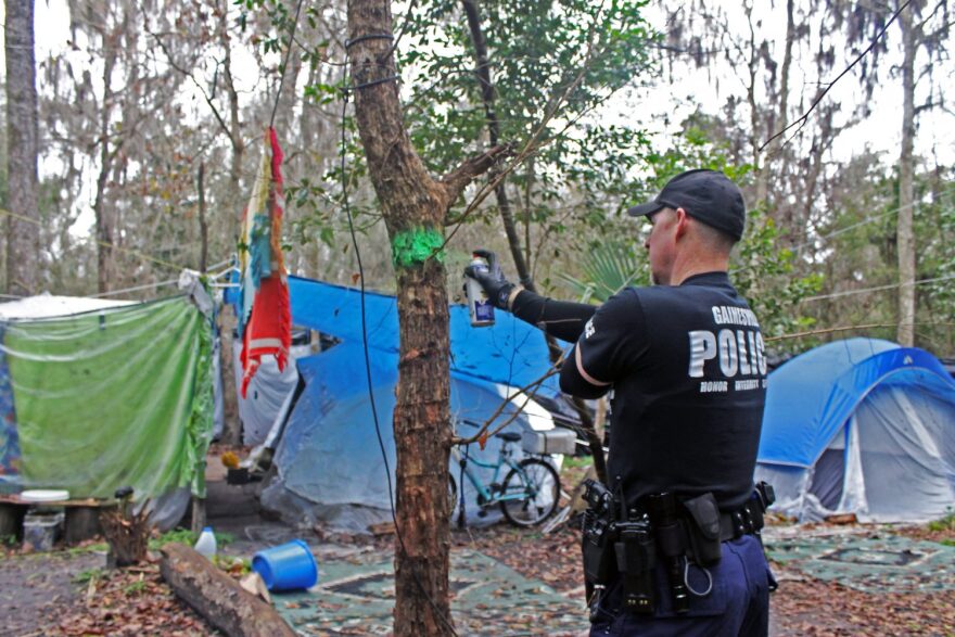 William Gough, a Gainesville Police Department officer, tags a tree with green spray paint in order to color-coordinate sections of Sweetwater Branch, a homeless community, during a zoning initiative implemented to improve emergency response times to homeless communities.