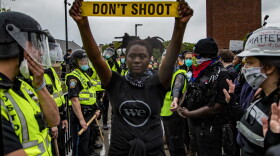 A protester holds up caution tape that read “Don’t Shoot” as police and protester stand off in front of Forest Hills station in Jamaica Plain im June 2020. (Jesse Costa/WBUR)
