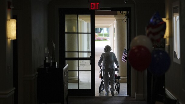 A woman uses a walker as she exits an assisted living building